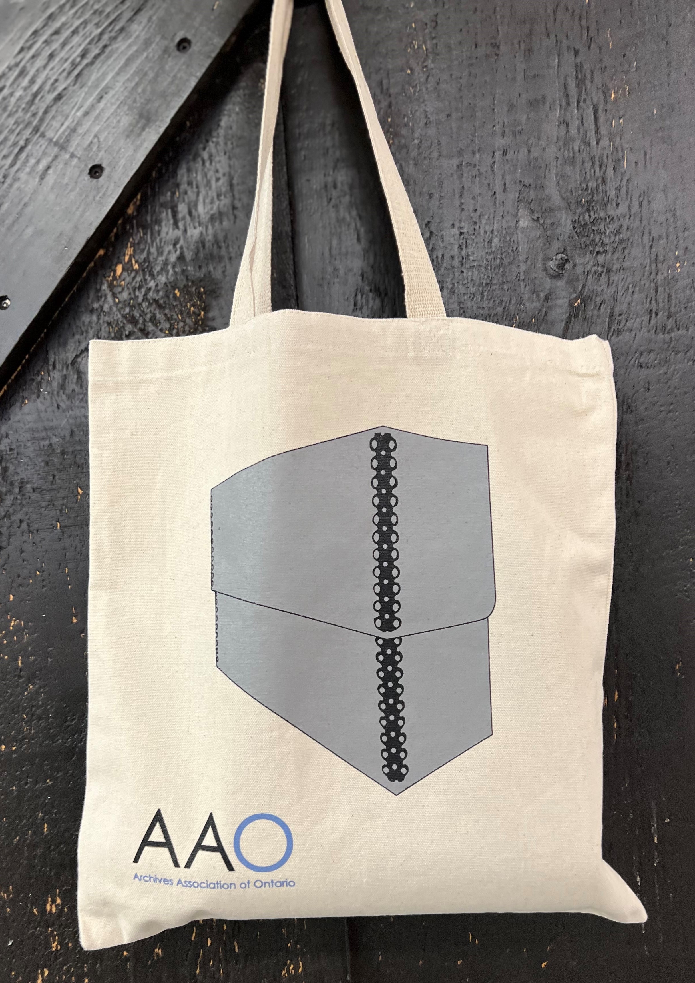 Tote bag with an image of a Holinger box un grey and black above the AAO logo.